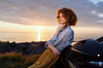 Fototapeta premium A woman gazes toward a sunset over the ocean, dressed in casual denim and a flowing skirt, capturing a contemplative lifestyle moment outdoors.