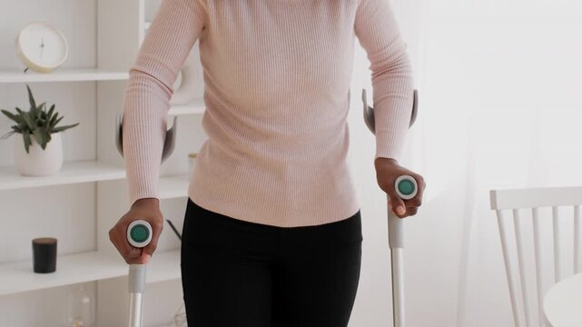 Positive African American Woman Using Crutches For Support While Standing At Home, Demonstrating Mobility Aids In A Living Room Setting. Empowering Sight For Healthcare Concept.