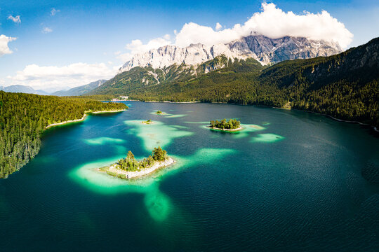 Aerial view of Eibsee lake with small islands and turquoise waters surrounded by dense pine forests and the towering peaks of the Zugspitze massif in Grainau, Bavaria, Germany.