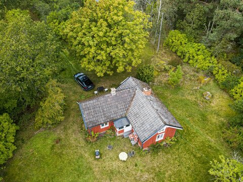 Aerial view of a traditional red Swedish house with a grey tiled roof surrounded by lush green trees and grass in Oland, Jonkoping County, Sweden.