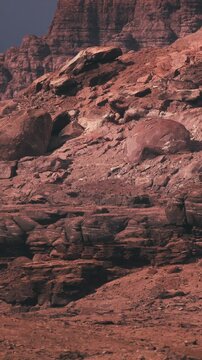 The scene shows red rocks and mountains in a desert setting during sunset. The sun casts shadows on the rugged terrain, highlighting the unique shapes of the rocks.