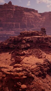 The scene captures rocky formations and dry ground under a clear blue sky. The sun shines brightly, showcasing the texture of the stones. There are no plants or water in sight.