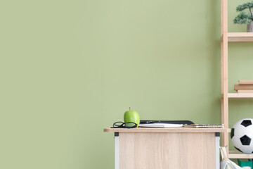 Fototapeta premium Apple with eyeglasses on desk near green wall in classroom
