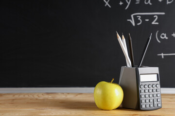 Obraz premium Apple, calculator and pencils on desk near chalkboard with formulas. Back to school concept