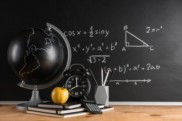 Obraz premium Apple, globe, alarm clock and stationery on desk near chalkboard with formulas. Back to school concept