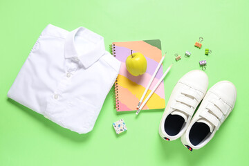 Fototapeta premium Tasty apple, shirt, shoes and different school stationery on green background
