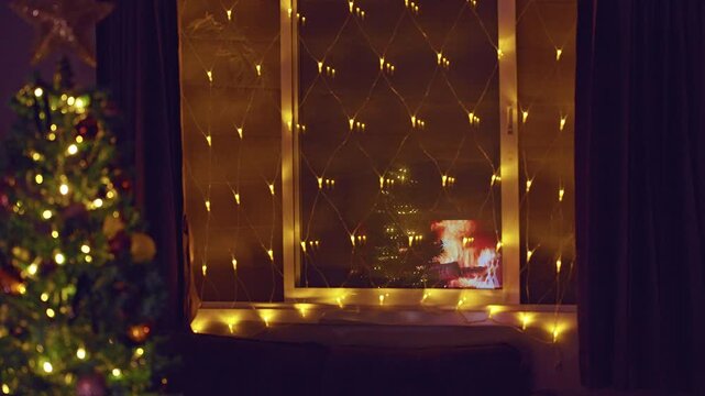 Warm Christmas Window Decorated With Golden Fairy Lights Reflecting a Cozy Fireplace and Christmas Tree, Festive Holiday Interior, Peaceful Winter Evening