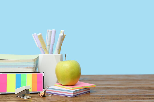 Pencil holder, sticky notes, different school supplies and green apple on table against blue background