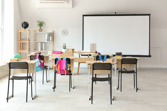 Interior of light classroom with projector screen and desks