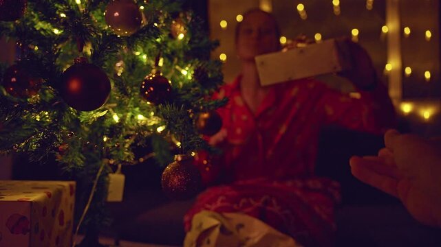 First Person View Offering a Wrapped Christmas Gift to a Happy Woman Beside a Decorated Tree With Warm Fairy Lights, Cozy Holiday Home, Giving and Family Love