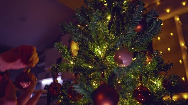 Close Up of Hands Decorating a Christmas Tree With Glowing Ornaments and Warm Fairy Lights, Cozy Holiday Tradition, Festive Home and Winter Celebration