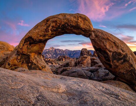 A majestic natural rock arch stands against a vibrant sunset backdrop with distant mountains
