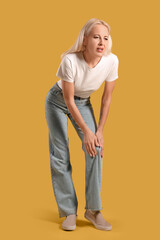 Fototapeta premium Mature woman suffering from knee pain on yellow background