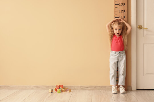 Shocked little girl measuring height near wooden stadiometer