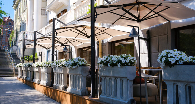 A summer street scene with a charming street cafe featuring a row of tables and chairs, inviting passersby to immerse themselves in the cafe's urban culture.