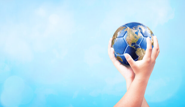 Hands holding planet earth globe soccer ball with copy space on soft blue bokeh background for global sports and peace banner design