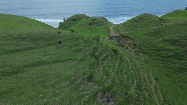 Woman Walking Ridge With Ocean View, Narrow Grassy Paths Snake Between Rolling Knolls Toward Distant Cove, Cinematic Composition With Moody Sea Horizon, Solitary Hike,Bukit Merese, Lombok, Tanjung Ann