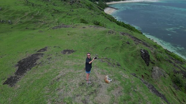 Woman Photographing Coastal Green Ridge with Mobile Phone, Wide Ocean Panorama, Dramatic Cloudy Sky, Island Silhouettes, Standing On Summit, Content Creator Pose, ,Bukit Merese, Lombok