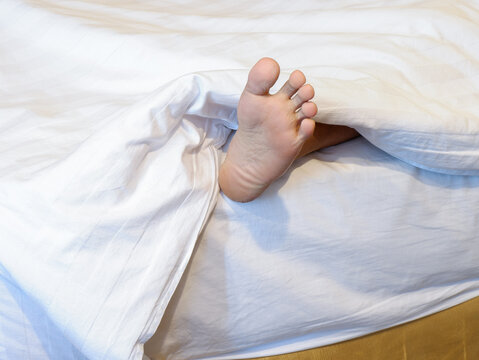 ​Dead body foot sticking out from under white sheet on bed, crime scene investigation and forensics concept