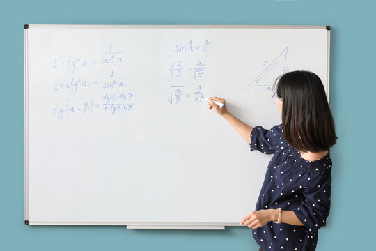 Asian Math teacher near flipboard in classroom