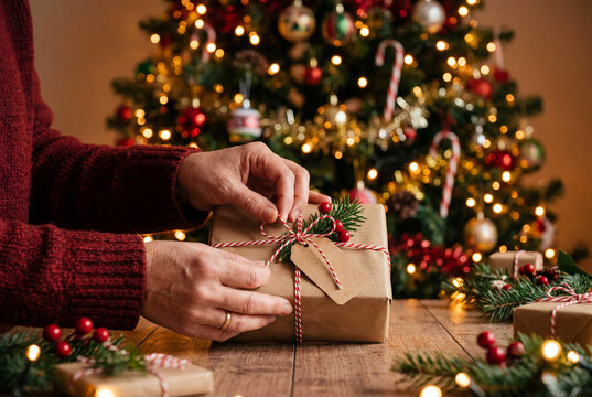 Woman hands in red sweater tying string on a wrapped christmas gift box