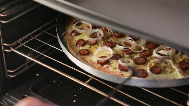 POV: pizza maker checking the pizza inside the oven. Chef rotates the pizza with a spoon. Close-up: Pepperoni, mozzarella, and onion pizza baking in the oven. Making pizza. Homemade pizza. Pizza day.