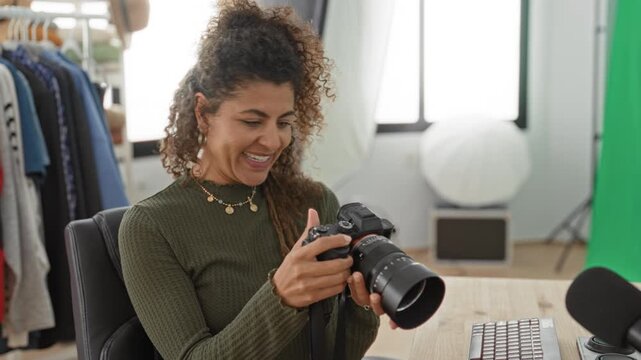 Woman holding camera and checking images on the camera screen while smiling in studio surrounded by clothing rack and lighting; excitement creativity.