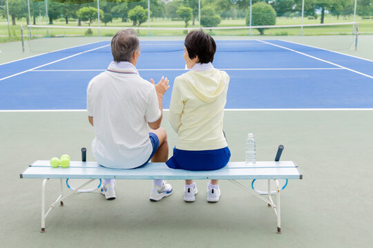 テニスコートのベンチで休憩するシニア夫婦の後ろ姿