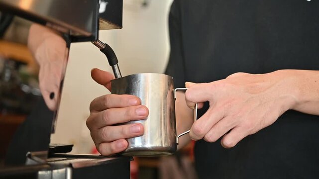 Barista using espresso machine for steaming milk. A milk steamer is a device used to heat milk and is commonly found attached to espresso machines.