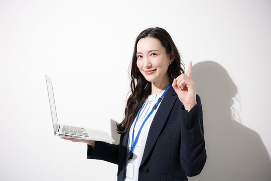 ノートパソコンを持つ笑顔の日本人ビジネス女性、DXやAI、業務改善、ITサービスをイメージしたビジネス上半身クローズアップ　カメラ目線の指差しやポイントのオススメや紹介のポーズ