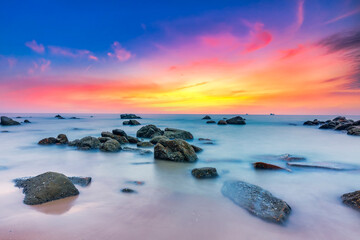 Naklejka premium Beautiful coastal sunrise scene featuring a dramatic rock formation rising from a sandy beach. 