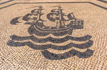 Traditional black and white stone pavement with a sailing ship mosaic in Lisbon, Portugal. © Kavalenkava
