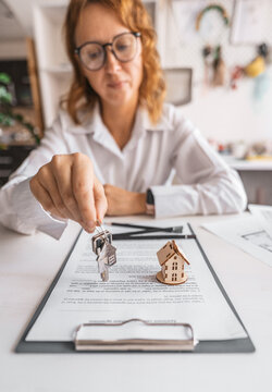 Real estate agent presents house keys and miniature home above signed documents and floor plans. Concept of successful property purchase, ownership transfer and beginning of comfortable new life.