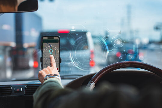 Driver pointing at smartphone navigation map on dashboard with futuristic digital hologram HUD overlay in car.