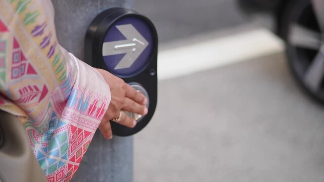 Person presses button at a crosswalk in a city street