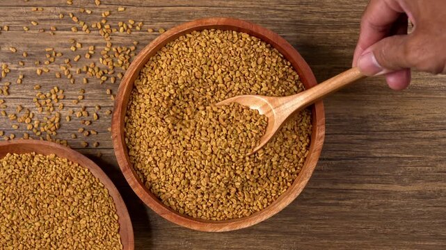 Top down view of scooping fenugreek seeds from a wooden bowl