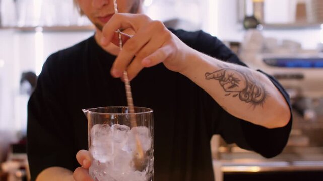 Barkeeper work. Refreshing drink. Man stirring ice cubes in glass pitcher with long bar spoon making chilling cocktail on pub counter.