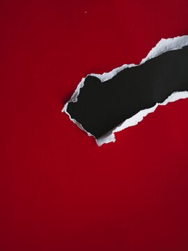 A diagonal rip in red paper revealing a black background underneath.