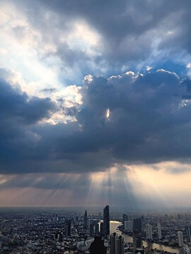 Dramatic sun rays breaking through dark storm clouds over a modern city skyline.