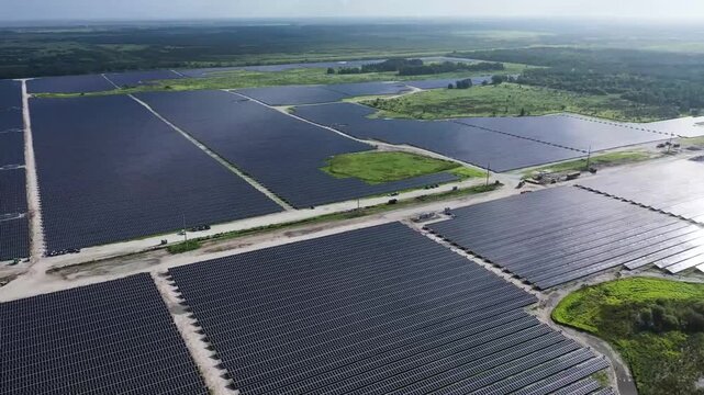 A cinematic drone shot soaring above an expansive solar energy farm, capturing endless rows of solar panels converting sunlight into clean, renewable power. The aerial perspective emphasizes the scale