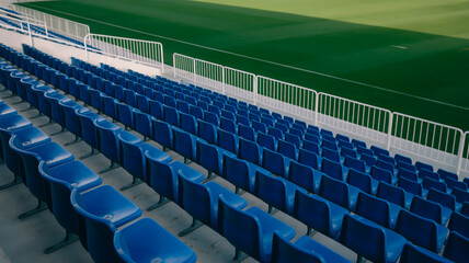 Naklejka premium Rows of empty blue stadium seats in a sports arena with a green field visible in the background