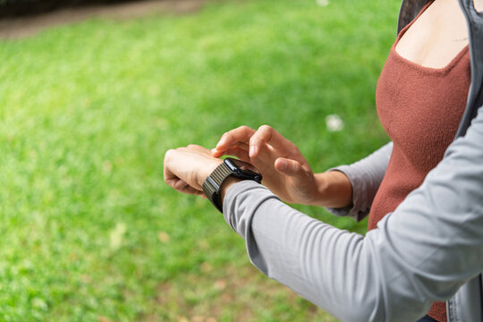 Asian Gen Z woman using smartwatch to track fitness activity during outdoor workout for wellness and healthy lifestyle.