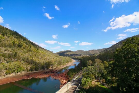 A beautiful high-angle view looking down at a rocky river winding through green hills under a bright blue sky at Somerset Dam in Queensland, Australia.