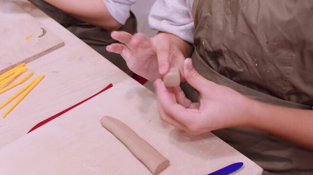 Artisan lesson. Clay modeling. Two creative unrecognizable children hands forming molding raw using pottery color tool in professional art workplace.