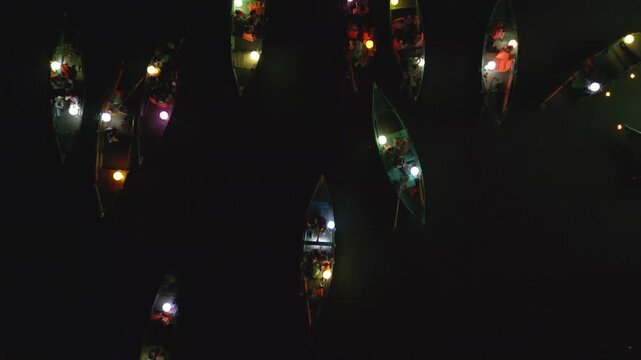Top down medium aerial view of boats with colorful lanterns passing by at night on the Hoi An river