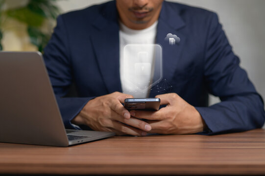 Businessman Sitting at Desk Using Smartphone with Laptop in Office Setting