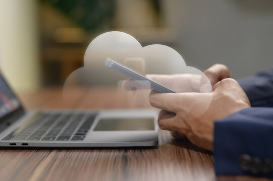 Business person using mobile phone with cloud and laptop on wooden desk
