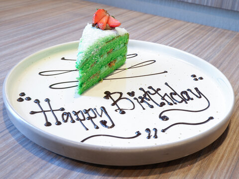 ​Pandan klepon cake slice with happy birthday chocolate writing on a white plate, celebration dessert serving close up