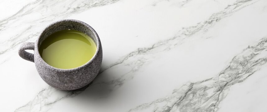 A textured grey ceramic mug filled with frothy green matcha tea on a white marble surface with grey veins