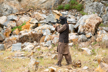 Fototapeta premium Armed militant aiming a rocket launcher during a simulated conflict scenario in rocky outdoor terrain